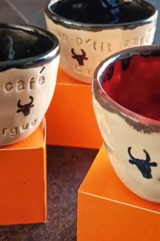 Trois bols artisanaux en céramique crème, bord noir. Avec symboles taureau et textes 'café', 'un p'tit café'. Sur blocs oranges.