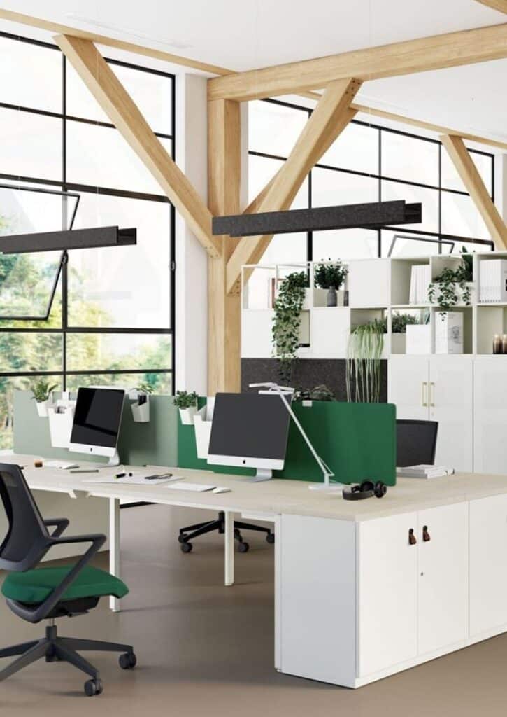 Bureau moderne avec grandes fenêtres, poutres en bois apparentes, postes de travail avec écrans, cloisons vertes et plantes.