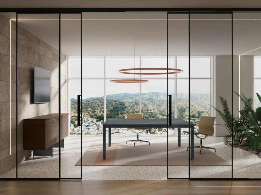 Bureau moderne avec portes vitrées, table de réunion, et vue imprenable sur les montagnes. Mur en pierre avec TV et meuble en bois, éclairage intégré.