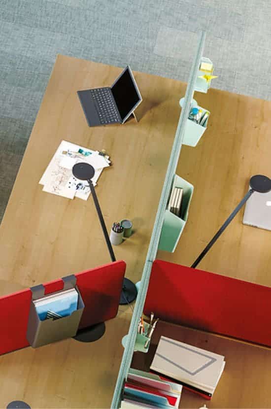 Vue aérienne d'un bureau moderne avec deux postes de travail en bois séparés par une cloison organisée. Ordinateurs portables, lampes et rangements intégrés visibles.
