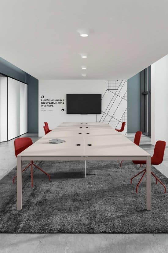 Salle de réunion moderne avec grande table beige équipée de ports, chaises rouges et téléviseur. Citation: 'Limitation rend l'esprit inventif. Walter Gropius'.