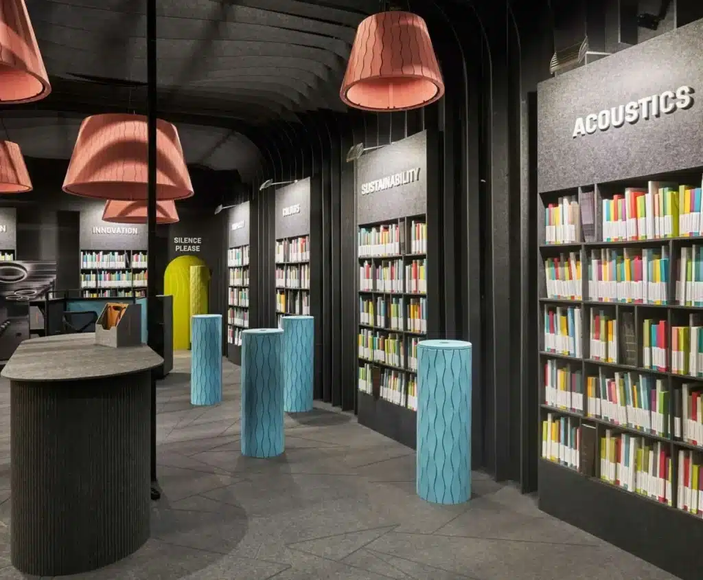 Intérieur de showroom sombre avec étagères "ACOUSTICS", "SUSTAINABILITY", "INNOVATION", "COLOURS", "SILENCE PLEASE". Lampes pêche, colonnes bleues texturées.
