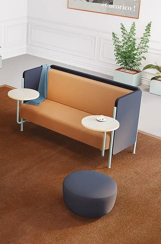 Sofa moderne marron avec tables intégrées, pouf bleu. Mur lambrissé blanc, plantes vertes, cadre « #Cocoricco ! ».