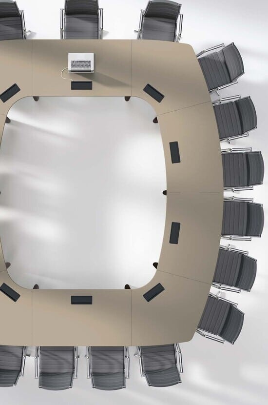 Grande table de conférence beige en U avec chaises grises, vue d'en haut. Un ordinateur portable est posé au centre d'une section.