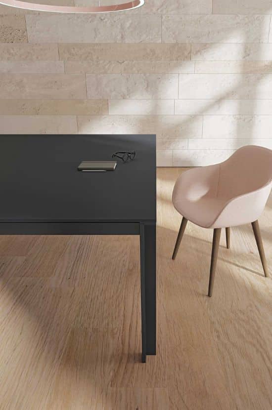 Table noire moderne avec smartphone et lunettes, sol parquet clair, mur en pierre beige, et chaise rose élégante.